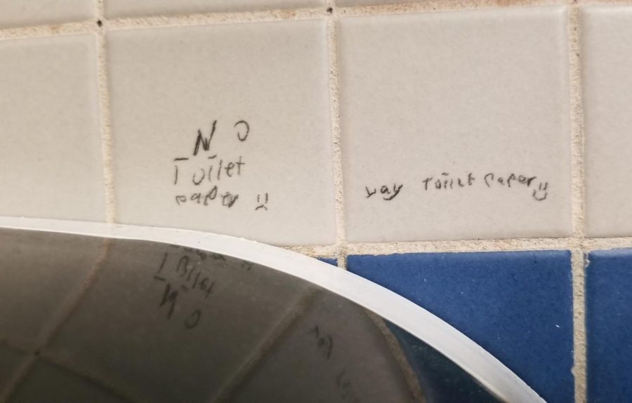 Writing above the toilet paper in a stall. The comment on the left reads  No toilet paper :(, and the comment on the right says Yay toilet paper :).