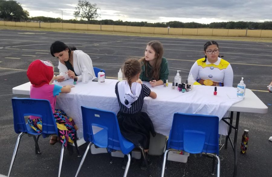 Three students sitting at a table where two children are getting their nails painted.