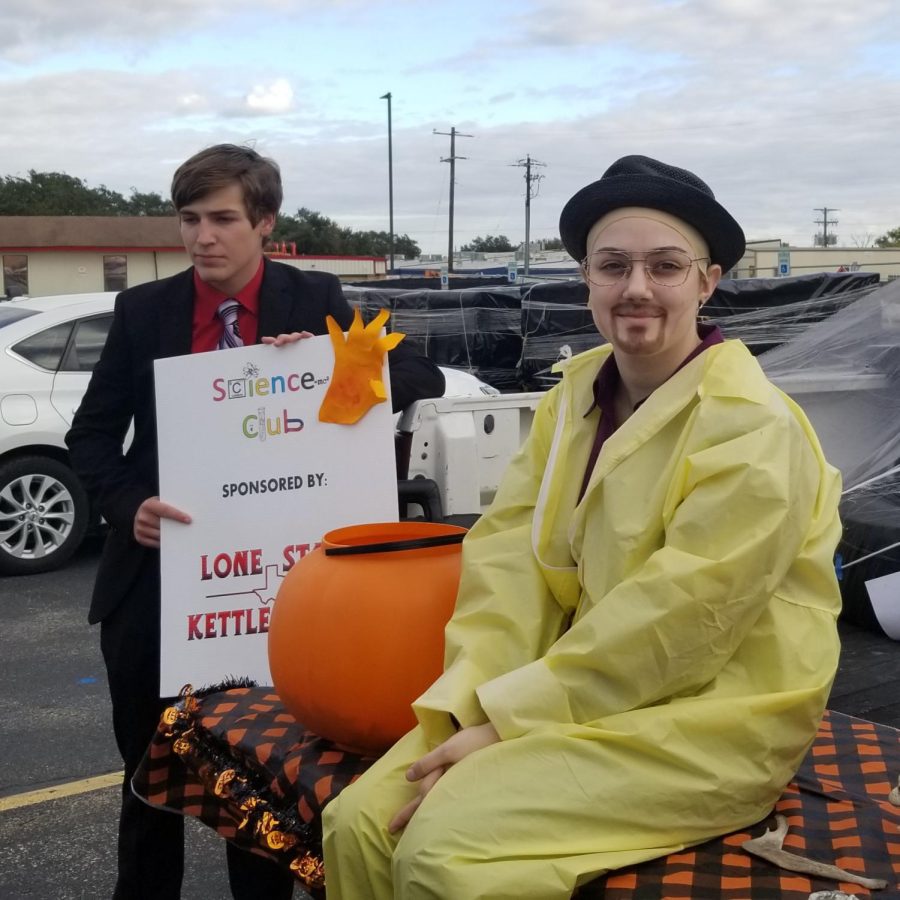 A student dressed as Saul Goodman holding a Science Club sign and a student dressed as Walter White sitting next to the candy bucket.